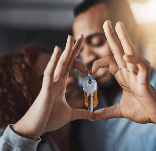 A smiling man and woman hold a home key with their thumb and index finger in the shape of a heart