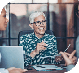 An older woman with glasses holds a form and smiles at a banker