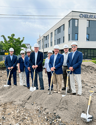 6 men and 2 women in blue blazers and white construction hats holding shovels and standing on a pile of dirt outside of Nebula Trust Bank