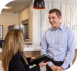 A man in a blue collared shirt smiles down at a woman in a black blazer holding a closed tablet inside of Nebula Trust Bank