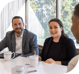 Two people sitting at a conference table smile at a man in the foreground