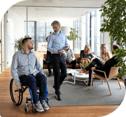 A young man in a wheelchair looks up at an older man walking alongside him with people in chairs in the background