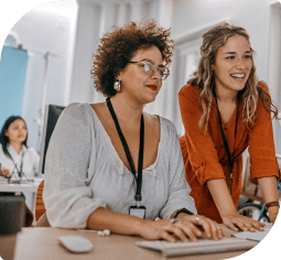 Two smiling woman, one sitting one standing, look at a laptop screen