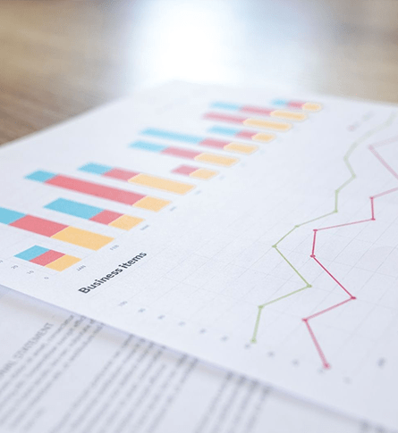 A piece of paper with a blue, red, and yellow bar graph, and a green and red line graph titled "Business Items" rests atop a white peace of paper with blurred black text