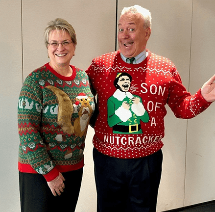 June Holaday smiling in a green Christmas sweater with her husband smiling in a red Christmas sweater