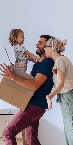 A young child smiling at a man and woman is carried in a large box