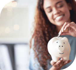 A woman smiles while putting change in a piggy bank