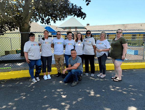 9 smiling people in white ONE Forte t-shirts outside of a playground