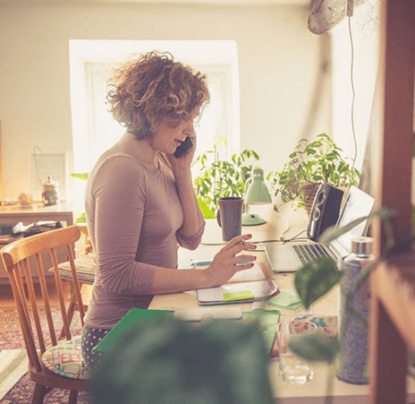 A worried woman sitting at a table with a laptop and notebook speaking on the phone