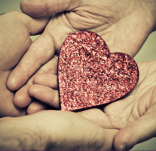 Two pairs of hands cradle a sparkly red heart