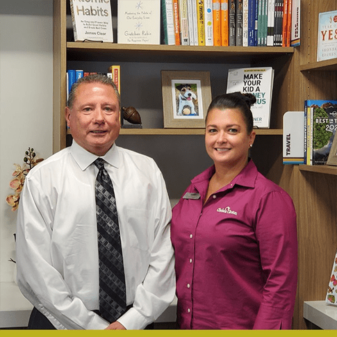 Kerri McGrath in a pink shirt smiling with an older man in a while shirt and black tie in a librar