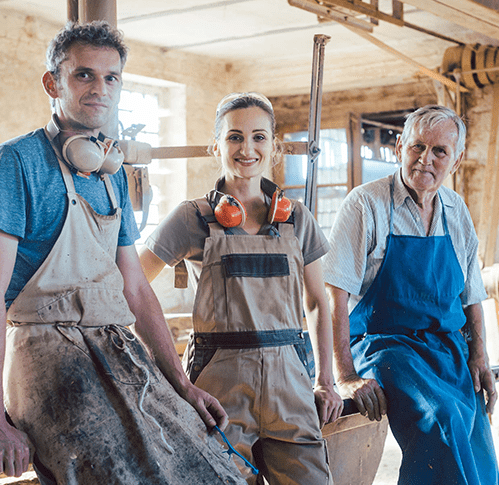 Two men and a women smiling wearing blue and brown coveralls and headphones inside of a workhouse