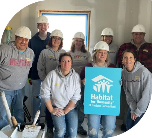 Nine volunteers with white hardhats hold a blue habitat for humanity of Eastern Global sign